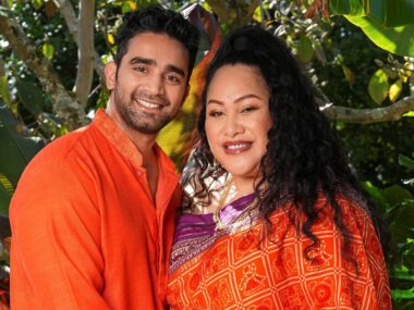 Bella and partner Suraj both wearing orange standing together in front of a bush