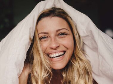 Woman smiling with duvet cover over her head like a hat