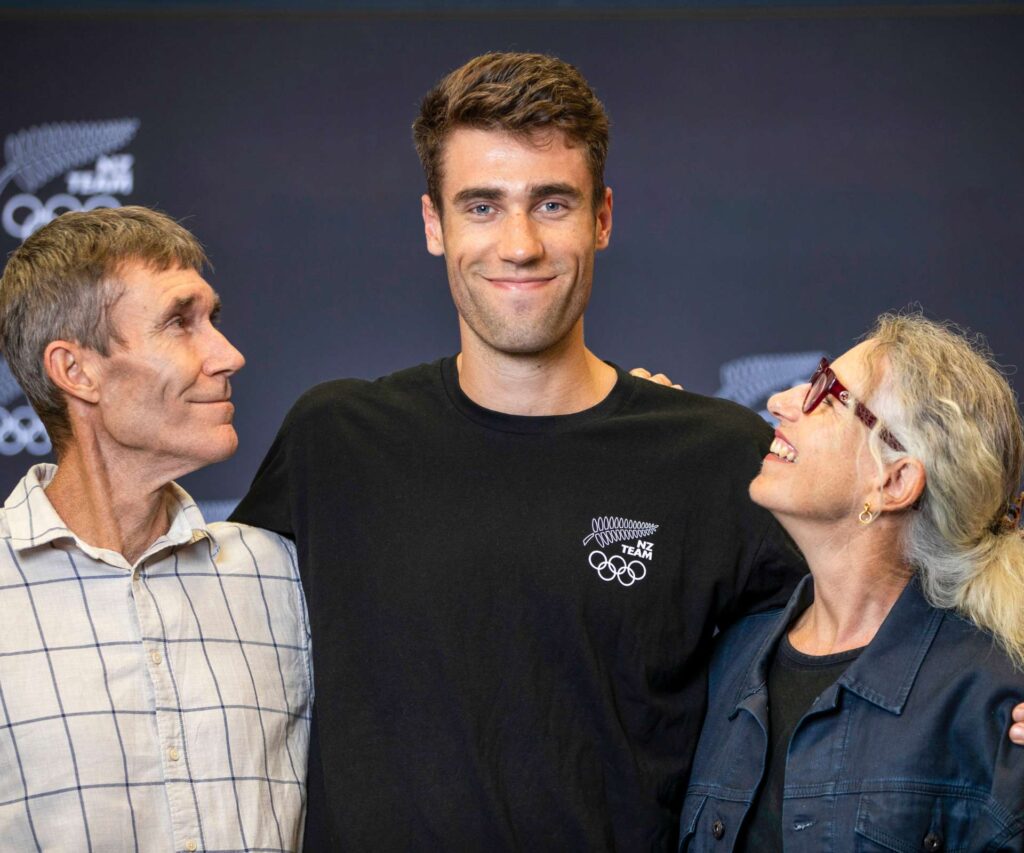 Hamish standing between his parents, both of them looking up at their smiling son