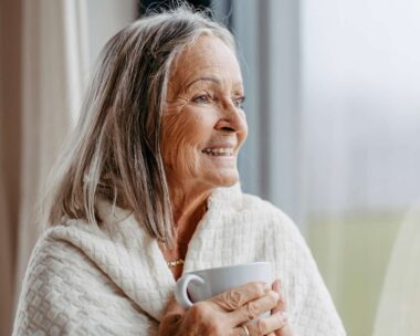 A woman looking out of a window holding a warm mug