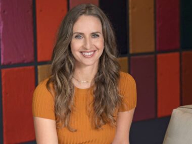 Fleur Saville smiling in front of a checkered background with different shades of red